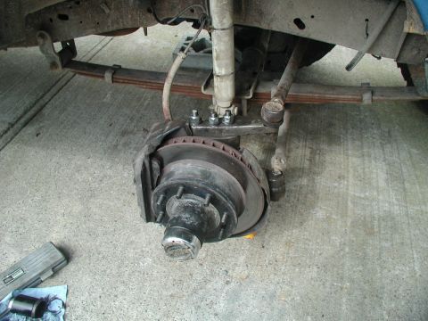 1985 Ford Bronco - The underside of a vehicle, likely a Ford Bronco, shows the front suspension and brake assembly during a repair. Leaf springs, a shock abso…