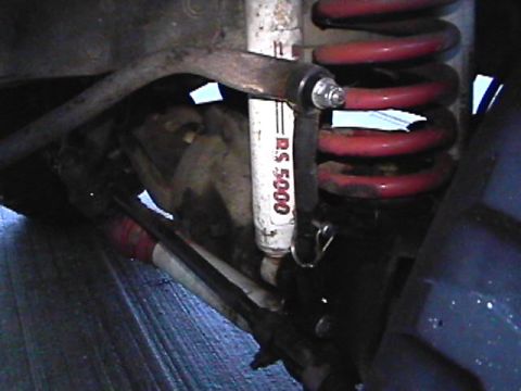 1985 Ford Bronco - A close-up view of the suspension components of a vehicle, featuring a red coil spring, a white shock absorber labeled "R.S. 5000", and par…