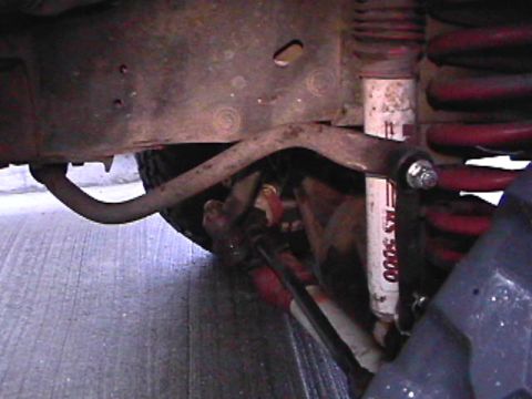 1985 Ford Bronco - A close-up, low-angle view of the front suspension components of a vehicle, including a sway bar, shock absorber, and coil spring. The shoc…