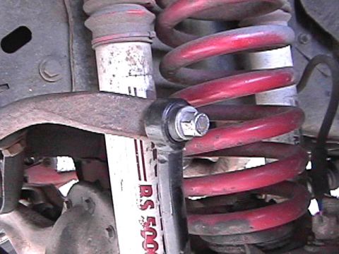 1985 Ford Bronco - This image shows a close-up of the suspension system of a vehicle, featuring a red coil spring and a white shock absorber with red letterin…