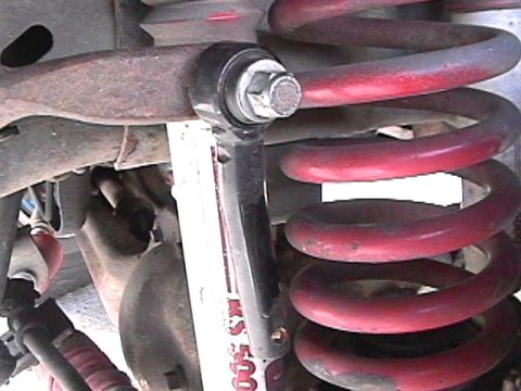 1985 Ford Bronco - A close-up view of the suspension system of a vehicle, featuring a red coil spring and a black sway bar end link with a silver bolt.