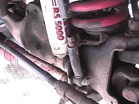 1985 Ford Bronco - A close-up, low-angle shot shows the suspension components of a vehicle, including a red coil spring, a white Rancho RS 5000 shock absorber…