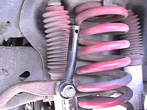 1985 Ford Bronco - A close-up view of the suspension system of a vehicle, featuring red coil springs and a black shock absorber assembly. A rusty metal contro…