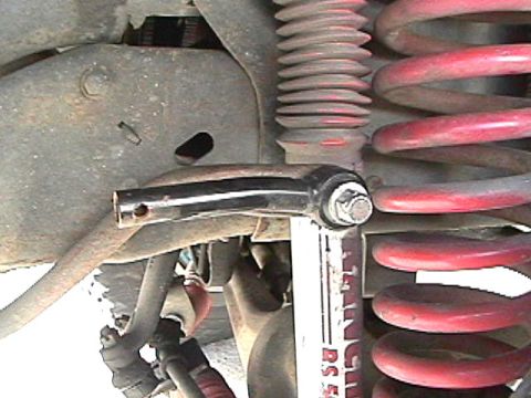 1985 Ford Bronco - A close-up view of the suspension system of a vehicle, showing a red coil spring, a shock absorber with white lettering, and a metallic lin…