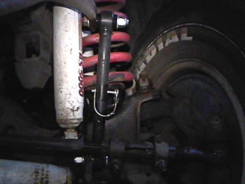 1985 Ford Bronco - A close-up view of the suspension components of a vehicle, including a white shock absorber with red lettering and a red coil spring, next…