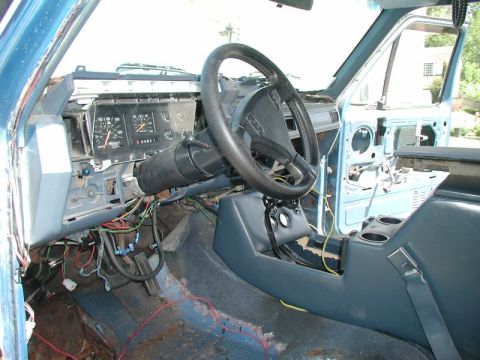 1985 Ford Bronco - The interior of a blue Ford Bronco is shown with the dashboard removed, revealing wiring and the steering column. The driver's side door is…