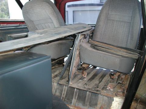 1985 Ford Bronco - The interior of a vehicle shows two gray fabric seats with a gray console or dashboard piece resting on top of them. The floor of the vehic…