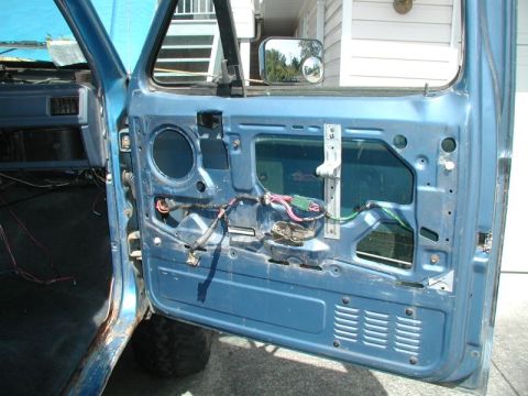 1985 Ford Bronco - The interior of a blue Ford Bronco's driver's side door is shown with the inner panel removed, revealing the window mechanism and wiring. T…