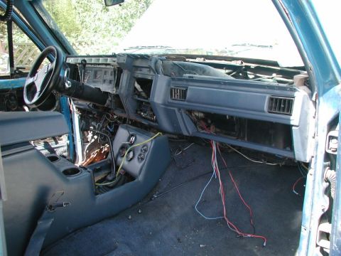 1985 Ford Bronco - The interior of a blue Ford Bronco is shown with the dashboard removed, exposing wiring and components. The steering wheel, center console,…