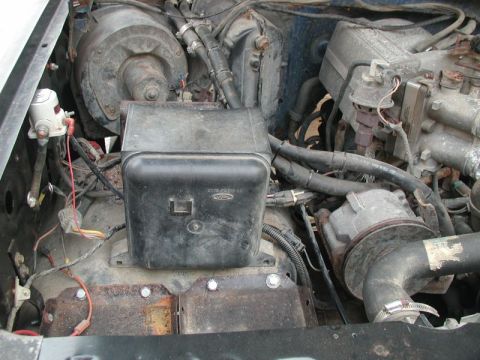 1985 Ford Bronco - A close-up view of the engine bay of a 1985 Ford Bronco, showing various engine components, wiring, and a black plastic air intake box.