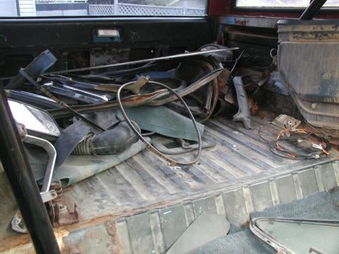 1985 Ford Bronco - The interior of a vehicle is cluttered with various car parts and debris. The floor and sides show signs of rust and wear.