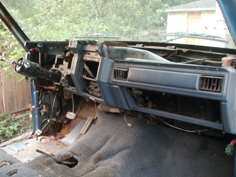 1985 Ford Bronco - The interior of a disassembled blue vehicle's dashboard is shown, with exposed wiring, rusted floorboards, and a steering column. The drive…