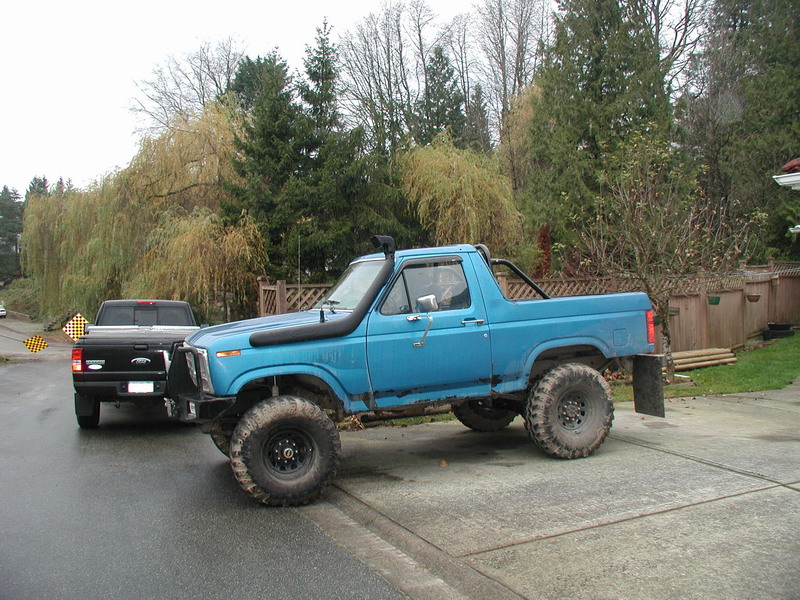 Lifted blue 1980s Ford Bronco with snorkel and large tires parked next to a black Ford Ranger.