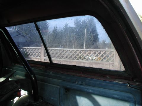 1985 Ford Bronco - Interior view of a vintage vehicle's rear window, showing a diamond-patterned fence and trees outside. A roll bar is visible in the foregro…