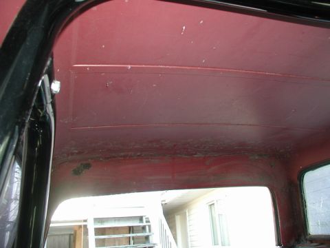 1985 Ford Bronco - Interior view of the red headliner and upper door frame of a vintage vehicle. The headliner has visible wear and some staining along the lo…