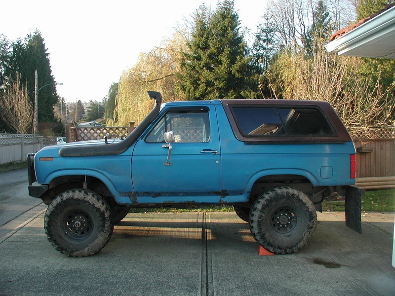 Blue 1980s Ford Bronco with snorkel and large tires, side view.