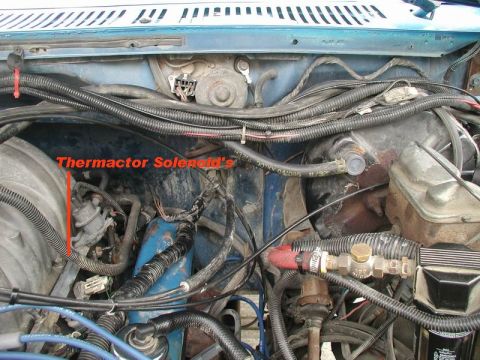 1985 Ford Bronco - The thermactor solenoid is visible in the engine bay of a blue Ford Bronco. Various hoses, wires, and engine components are also present.