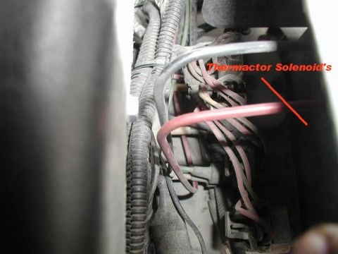 1985 Ford Bronco - A close-up view of a bundle of wires and connectors, with a red arrow pointing to a component labeled 'Thermactor Solenoid's'.
