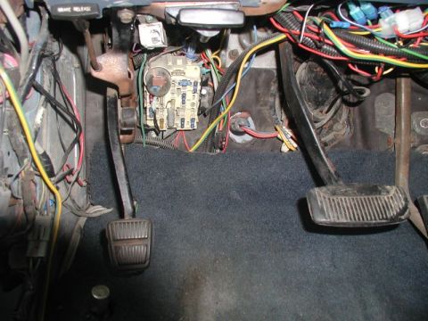1985 Ford Bronco - The interior driver's side footwell of an older vehicle shows the brake and clutch pedals, a fuse box with multiple fuses, and a complex wi…