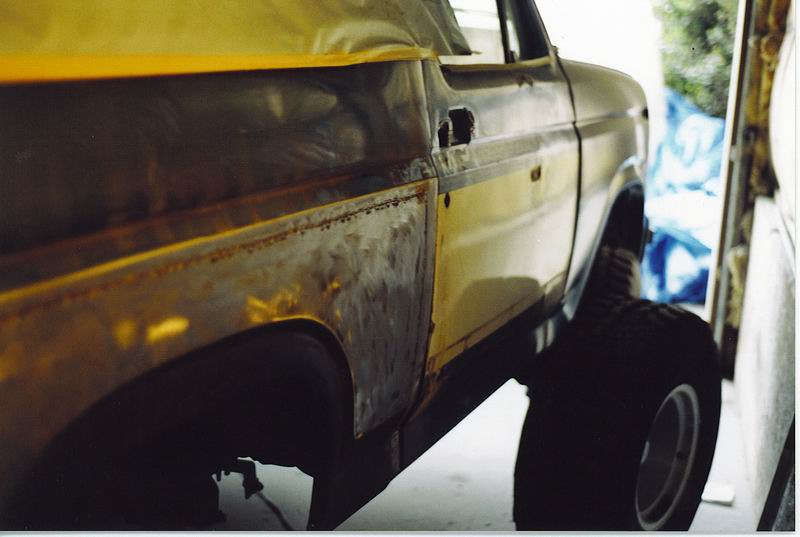 Yellow Ford Bronco side view, showing rust repair on quarter panel.
