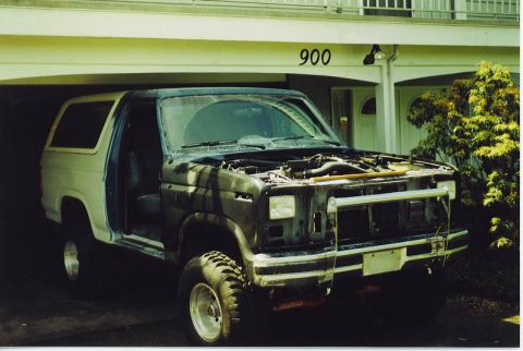 1985 Ford Bronco - A dark colored, two-door SUV is parked in a garage with its hood open. The vehicle appears to be undergoing some form of repair or modifica…