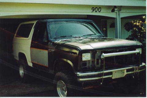 1985 Ford Bronco - A two-tone Ford Bronco is parked in a garage, with the front end partially disassembled. The vehicle is a dark brown and tan color, with or…