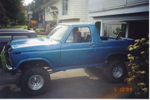 1985 Ford Bronco - A lifted, bright blue 1985 Ford Bronco is parked in a driveway in front of a house. The vehicle has large off-road tires and a custom front…