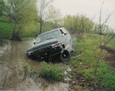 1991 Ford Bronco - Scanned print of a dark blue and silver Ford Bronco climbing out of a flooded creek at a steep angle, front wheels spinning on the muddy ba…