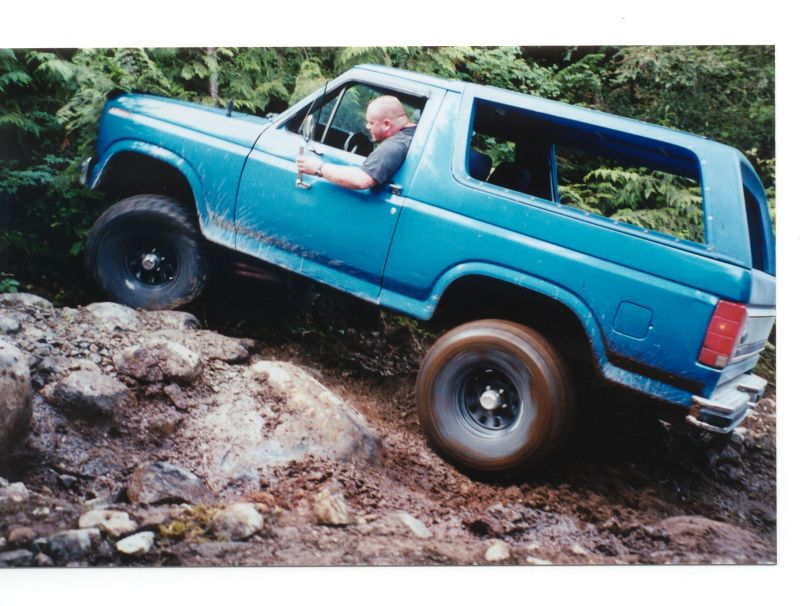 Blue Ford Bronco off-roading on a rocky, muddy hill.