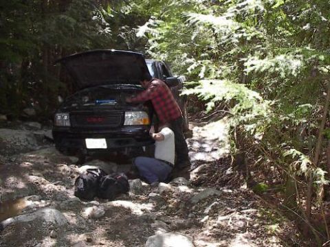 1985 Ford Bronco - I swear, it's not what it looks like. Jamie and Doug are getting a ratchet strap around Jamie's broken left motor mount.