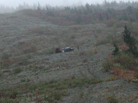 1985 Ford Bronco - Two vehicles are parked on a gravelly, overgrown hillside under a foggy sky. One appears to be a dark-colored SUV, possibly a Bronco, and t…