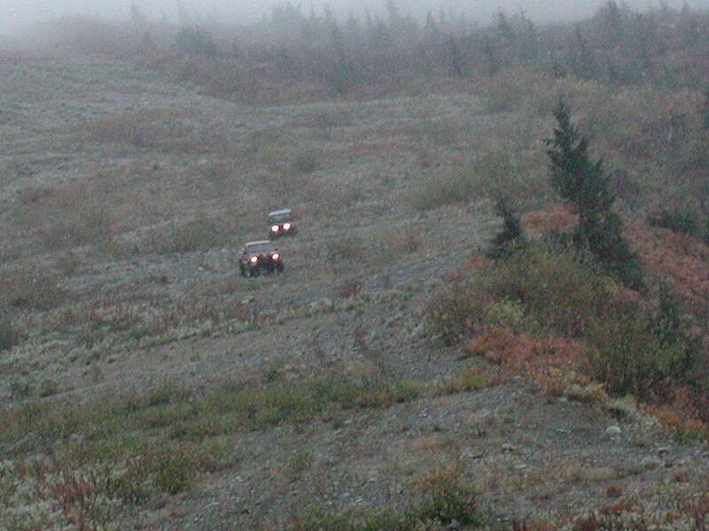 Two SUVs driving on a rocky slope in foggy conditions.