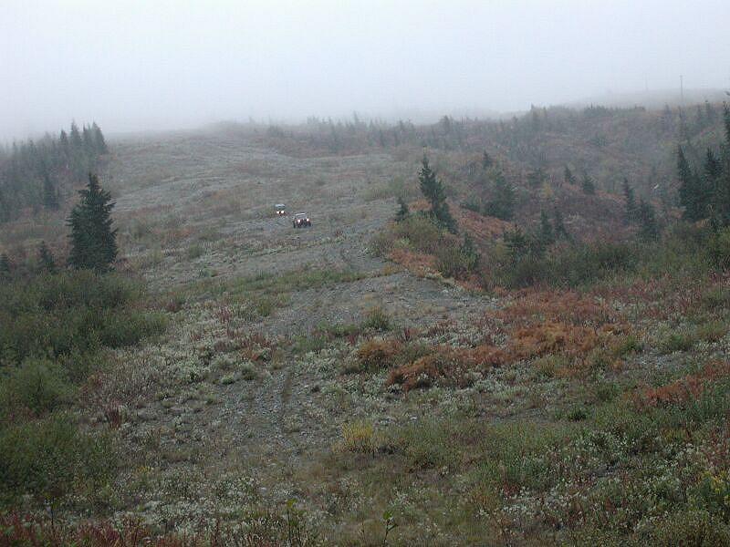 Two off-road vehicles on a gravel path in a misty, hilly landscape.