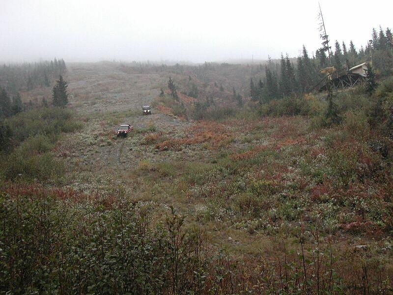 Two off-road vehicles on a muddy, rocky hill with a wooden structure on the right.