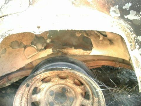 1985 Ford Bronco - Close-up view of the wheel well of a vehicle, showing damage to the fender liner and a rusty wheel with a leaf spring visible underneath.