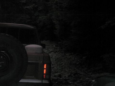 1985 Ford Bronco - The rear of a dark-colored SUV, possibly a Ford Bronco, is visible at night on a rocky, wooded trail. The spare tire is mounted on the rear…