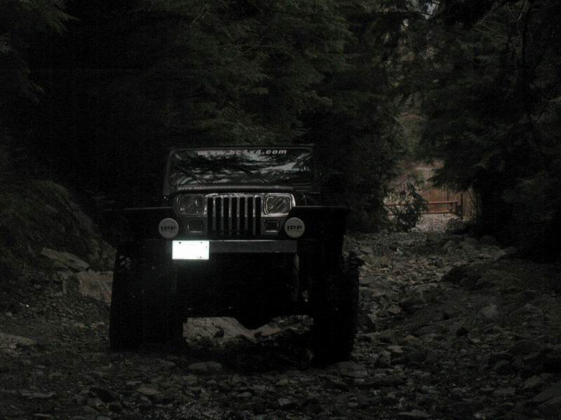Jeep Wrangler on a rocky trail in a dark forest.