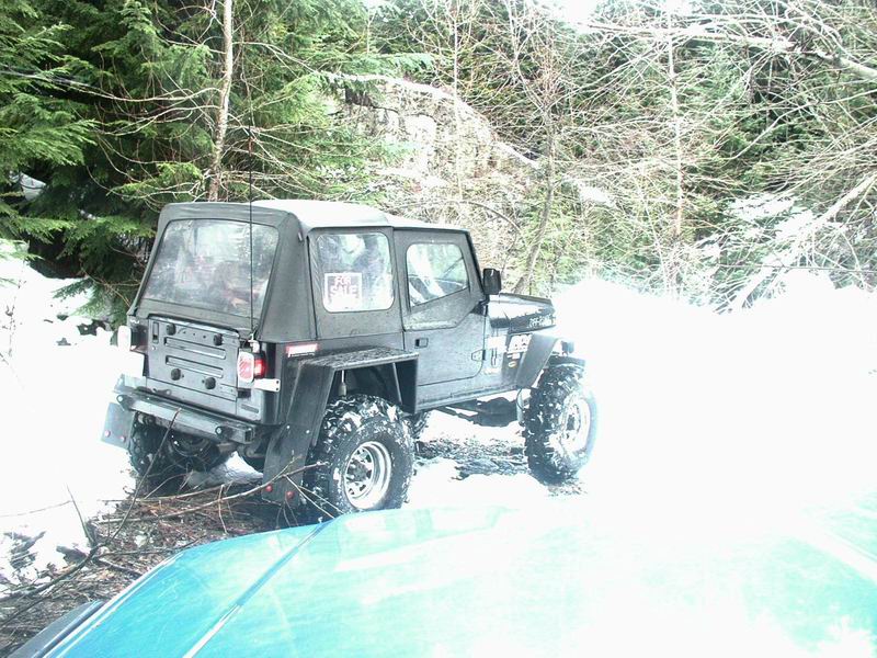 Dark Jeep Wrangler with soft top in snowy woods, "For Sale" sign in window.