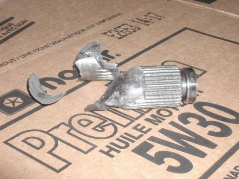 1985 Ford Bronco - A broken metal shaft with splines is shown on top of a cardboard box with oil viscosity information printed on it. The shaft appears to be…