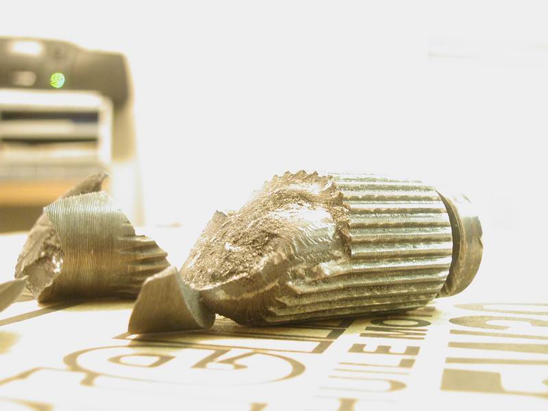 Two broken pieces of a metal ribbed object on a surface with text.