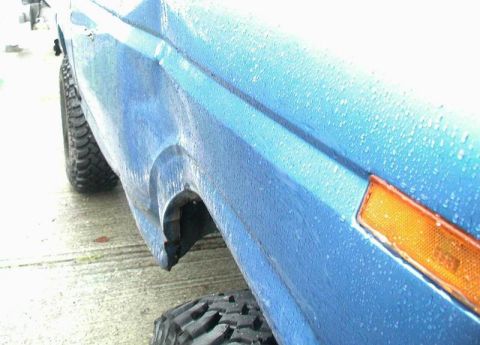 1985 Ford Bronco - A close-up, side view of a blue vehicle, possibly a Ford Bronco, with water droplets on its surface. The image focuses on the wheel well ar…