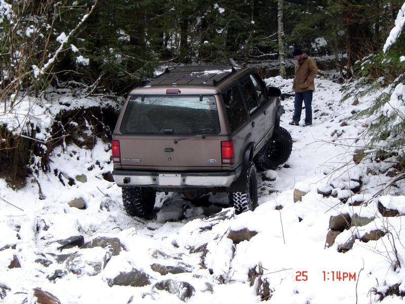 Tan Ford Explorer off-roading on a snowy, rocky trail in the woods.