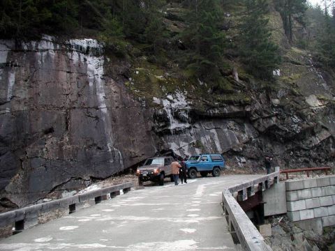 1985 Ford Bronco - Two SUVs are parked on a bridge next to a rocky cliff face. A brown SUV is on the right, and a blue SUV is on the left.