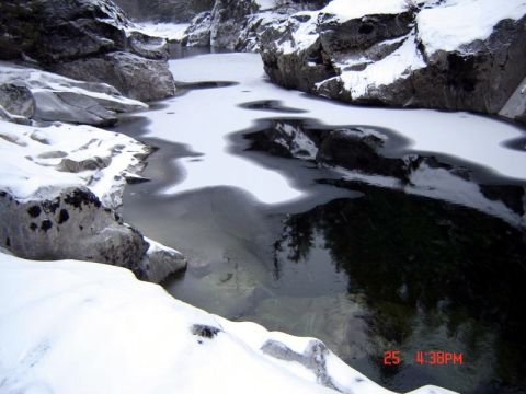 1985 Ford Bronco - A frozen river flows through a rocky canyon with snow on the banks and ice on the water. The reflection of trees is visible in the darker p…