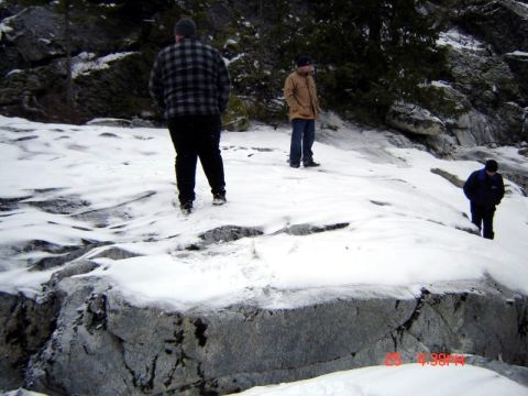 1985 Ford Bronco - Three people are walking on a snowy, rocky terrain near a wooded area. The person in the foreground is wearing a plaid jacket and dark pant…