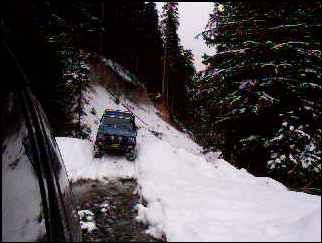 1985 Ford Bronco - A blue SUV navigates a snow-covered, wooded mountain road. The vehicle is seen from the perspective of another vehicle, looking forward and…