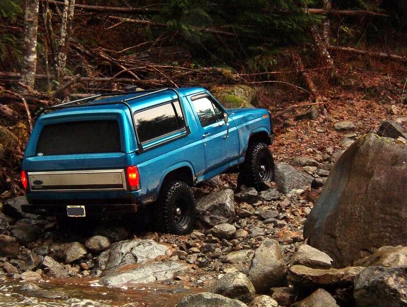 Blue 1985 Ford Bronco off-roading on a rocky trail