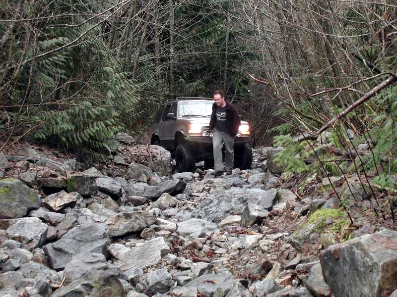 Silver Ford Bronco on a rocky trail with a man walking beside it.