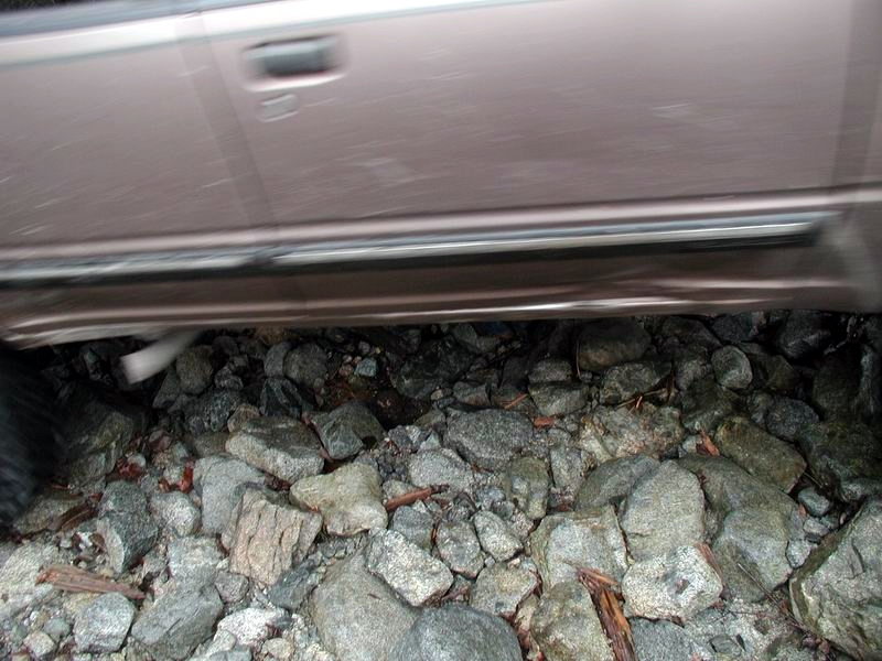 Tan SUV side view, parked over rocks, showing door, running board, and exhaust pipe.