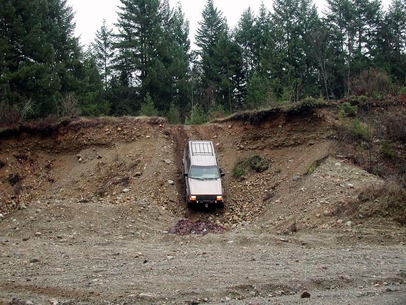 Tan SUV driving down a steep, rocky hill in a forest.